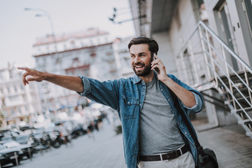 Portrait of beaming unshaven man gesticulating hand while speaking on mobile. He walking at street...