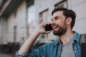 Side view outgoing unshaven male telling on mobile while walking on street during sunny day. Happy...