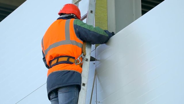 Worker, builder in orange a uniform and hard hat on the construction site, Installation sandwich panels. Finishing of unfinished building.