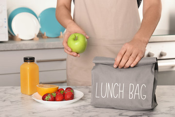 Woman packing food for her child at table in kitchen, closeup. Healthy school lunch