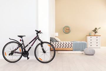 Bicycle near light wall in stylish room interior