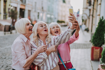 Obraz premium Happy stylish long-haired woman holding phone and making photo with hers friend outdoor