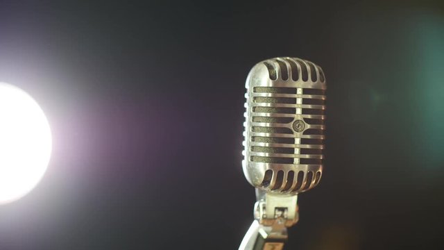 A vintage elvis microphone in front of a dark background with a stage light source in the corner. Shot in 4K