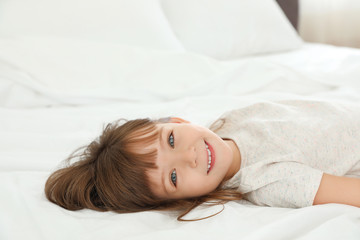 Portrait of cute little girl lying on bed at home