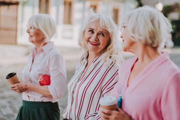 Waist up portrait of stylish older women drinking coffee and talking to each other while smiling