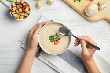 Woman eating fresh homemade mushroom soup from bowl on table, top view