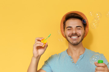 Young man blowing soap bubbles on color background. Space for text