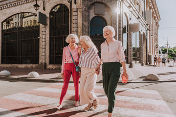 Full-length photo of three stylish adult women walking around the city while laughing