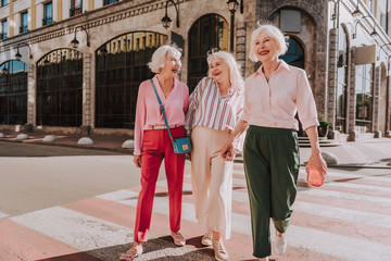 Full-length photo of happy older women are walking in center of city while having fun