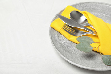 Plate with cutlery and napkin on light table, closeup. Space for text