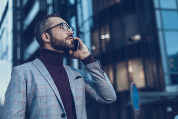 Bearded young man standing outdoors alone and looking into the distance while having important phone talk