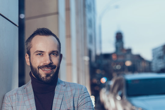Laconic portrait. Handsome bearded young man standing near the building outdoors and smiling