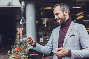 Staying connected. Emotional friendly young man standing outdoors with his modern smartphone and smiling while having video call