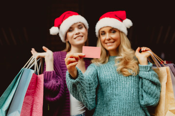 Waist up portrait of charming girl in santa hat enjoying shopping with mother. Focus on woman hand with credit card