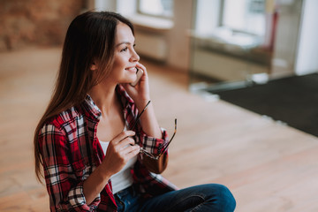 Side view portrait of beautiful girl having phone conversation and holding glasses. She is looking away and smiling