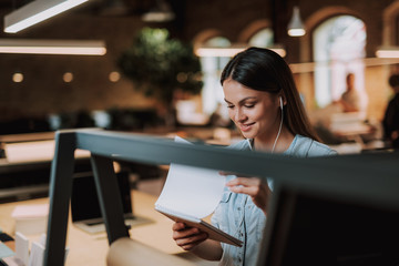 Portrait of beautiful woman listening music while looking at notebook. She is smiling