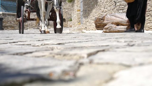 Low angle view of a horse drawn carriage passing two woman on a cobblestone road