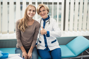 Obraz premium Concept of friendly relationship in therapist system. Waist up portrait of smiling female doctor and young woman sitting in medical office