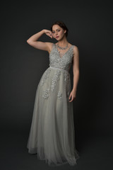 full length portrait of brunette  girl wearing long silver ball gown. standing pose on grey studio background.