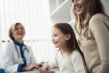 Concept of positive therapist consultation. Close up side on portrait of cheerful little girl and her mother sitting in pediatrician cabinet while consulting