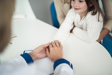 Concept of positive method of consultation in healthcare system. Top angle portrait of pediatrician woman holding hands of smiling female child while consulting