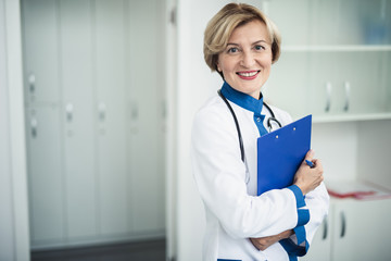 Concept of professional inspiration in healthcare system. Waist up portrait of smiling female doctor standing in medical cabinet with note holder. Copy space on left