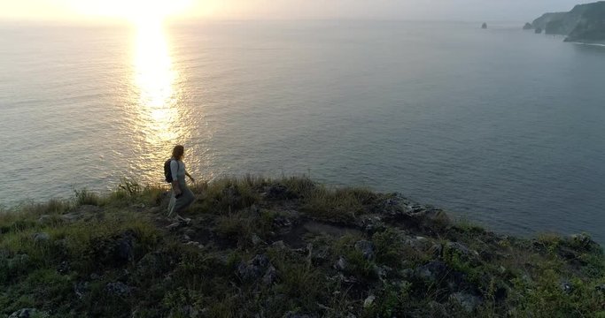 Aerial shot of girl travel photographer on edge of cliff taking photos of seascape 4K