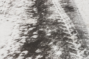 Slippery roads. Track from tire tread on snow. Textured winter background of asphalt with snowy drifts close up. Snowstorm on road with copy space. Abstract snowy weather texture. Snowfall in city.