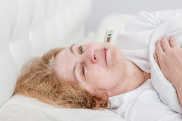 Close up sick senior woman with thermometer in mouth sleeping on the bed