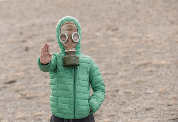 Boy in a gas mask on a deserted field showing stop gesture