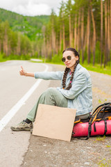 girl travels hitchhiking with a cardboard sign in her hands. Space for text