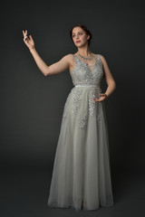full length portrait of brunette  girl wearing long silver ball gown. standing pose on grey studio background. © faestock