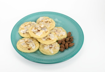 Homemade almond cookies and a bunch of whole almonds are on a teal colored plate against a white background.