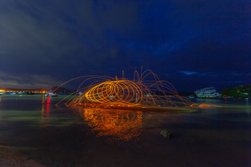 reflection of spark fire swirl from steel wool with long exposure speed motion abstract at sunrise in the sea