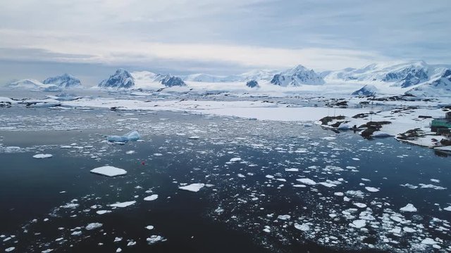 Aerial Flight Over Antarctica Snow Shoreline And Ocean. Drone Overview Of Polar Surface, Ice Frozen Ocean. Vernadsky Base On Antarctic Land. Snow Covered Mighty Mountains Background. 4k Footage.