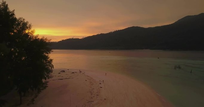 A beautiful sunset sky over ocean and distant islands is revealed by forward advancing, ascending aerial drone view around corner of forest, beach on tropical island Ko Lipe, Thailand. 4k 23.976fps