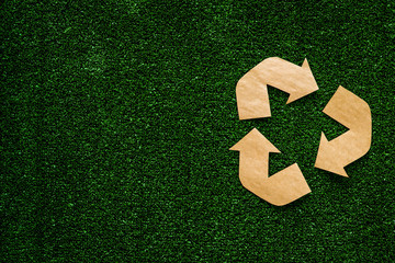 Eco recycle sign made of craft paper on green grass background top view copy space