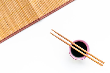 Chinese meal concept. soy sauce in bowl near chopsticks and bamboo table mat on white background top view copy space pattern