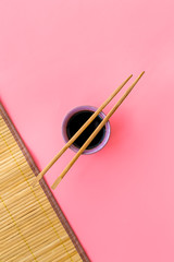 Chinese meal concept. soy sauce in bowl near chopsticks and bamboo table mat on pink background top view copy space pattern