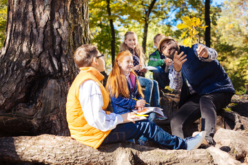 Forest fairytale. Delighted bearded man sitting near the tree while telling children an interesting story