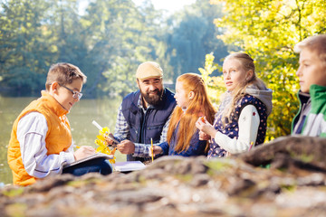 Beautiful nature. Nice young pupils sitting near the lake while exploring the forest together