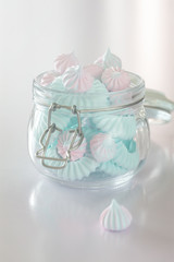 Light Pink and blue meringues in glass jar on pink background, vertical composition