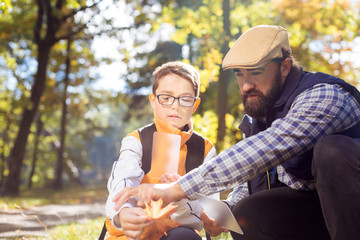 Nature photography. Pleasant bearded man sitting together with a boy while helping him to take a...