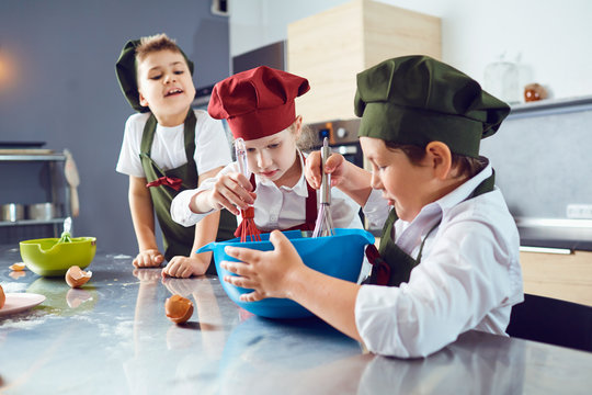 A group of children are cooking  in the kitchen.