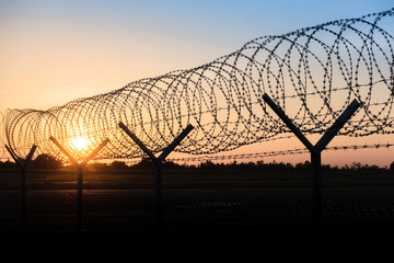 Silhouette of a barbed wire fence steel jail  with the sunset in the background