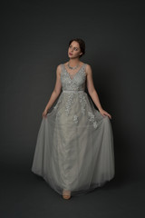 Fototapeta premium full length portrait of brunette girl wearing long silver ball gown. standing pose on grey studio background.