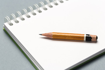 Short worn pencil with notepad on gray desk