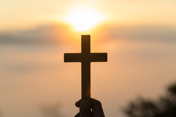 Silhouette of young  human hands praying with a  cross at sunrise, Christian Religion concept background.