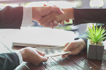Corrupted businessman sealing the deal with a handshake and receiving a bribe money, anti bribery...