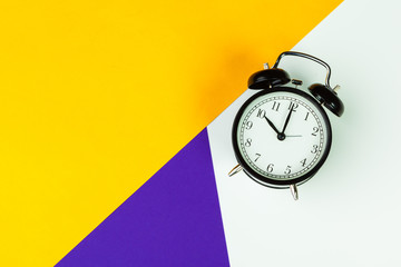 Black alarm clock on color block background, office interior